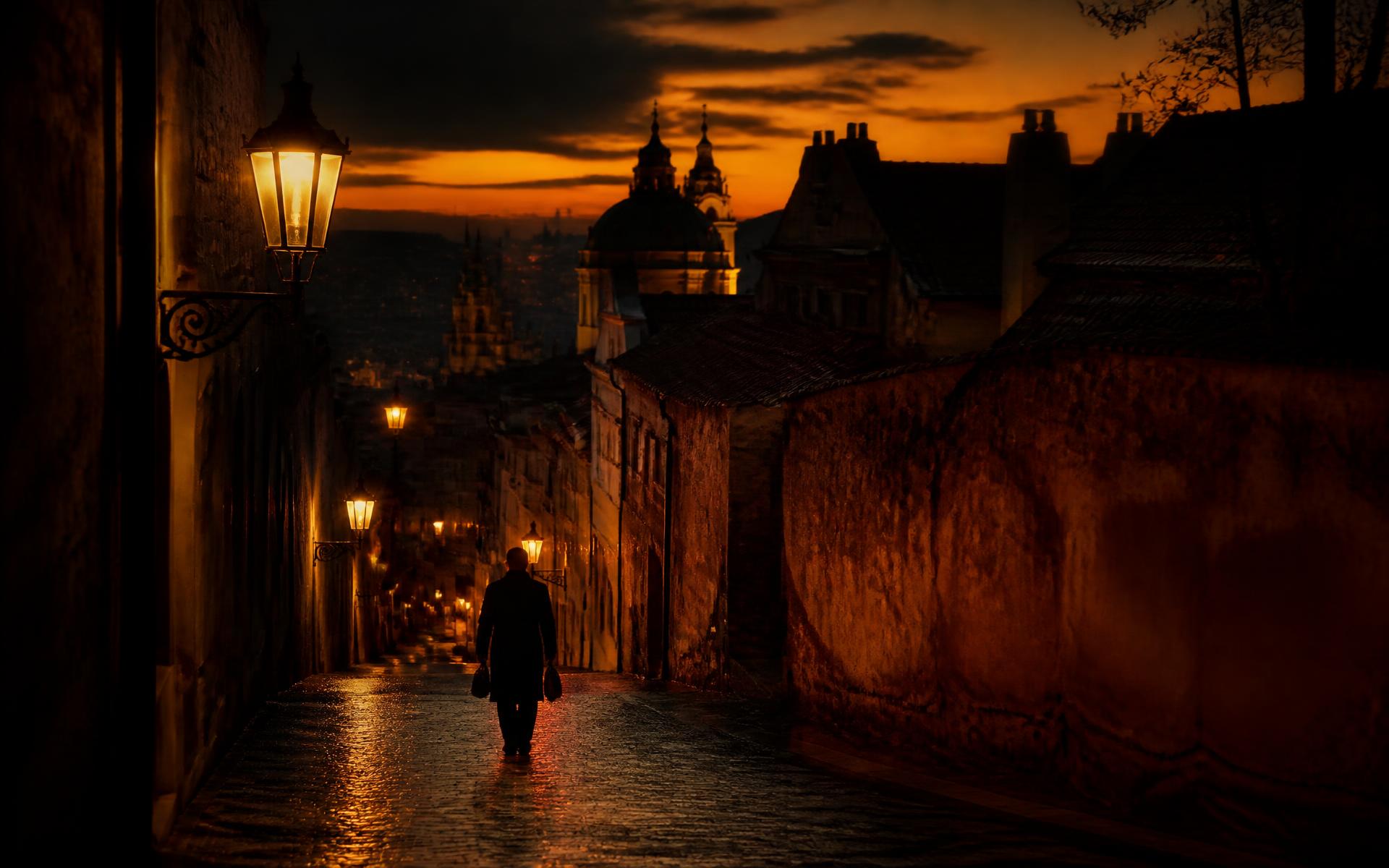 A lone traveller on a lamplit old-world street at golden dusk